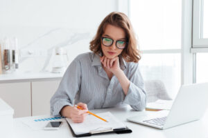 joven empresaria concentrada gafas camisa rayas trabajando papeles casa