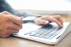 manos que sostienen tarjeta credito escribiendo computadora portatil